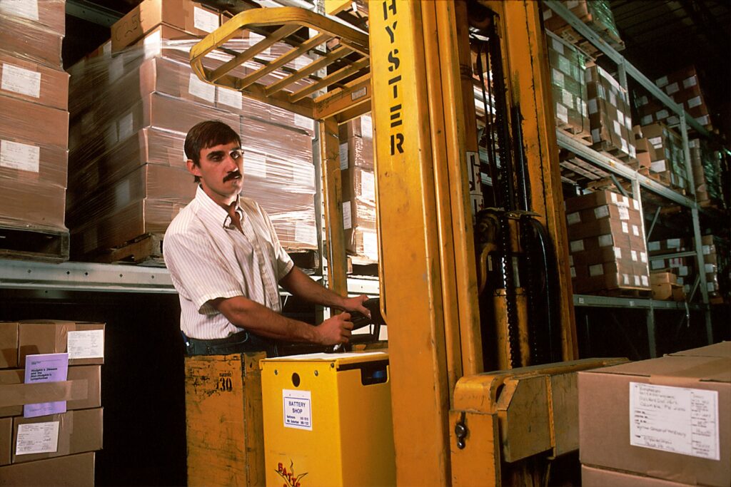 Operator mengemudikan forklift kuning di area gudang